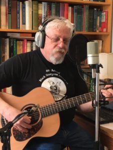 Cecil Burns wearing headphones, playing guitar and singing at a microphone.