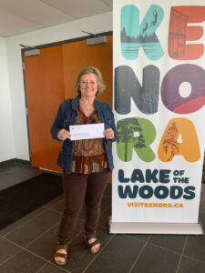 Woman holding an envelope in side a Kenora Lake of the Woods standup banner. 